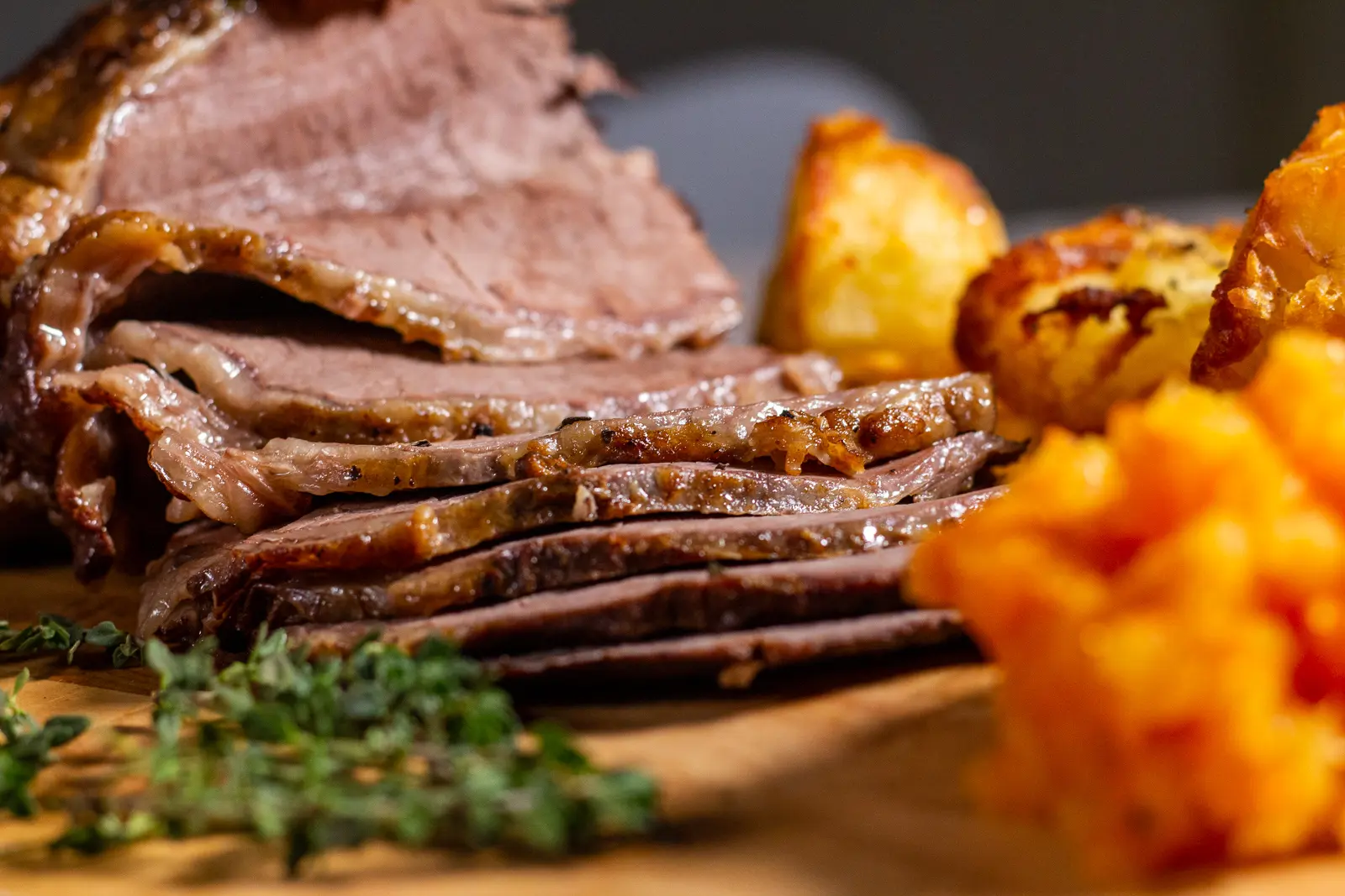 sliced slow cooked roast beef with roast potatoes in front